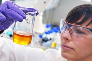 FUCHS Laborantin begutachtet ein Gefäß mit einer gelb-orangenen Flüssigkeit.