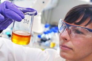 FUCHS laboratory technician inspects a vessel containing a yellow-orange liquid.